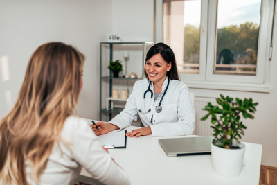 a female doctor seated at a white desk across from a younger female patient